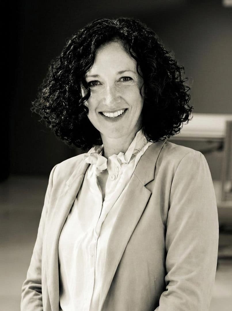 Smiling woman with dark curly hair wearing a light blazer in a sepia-toned portrait.