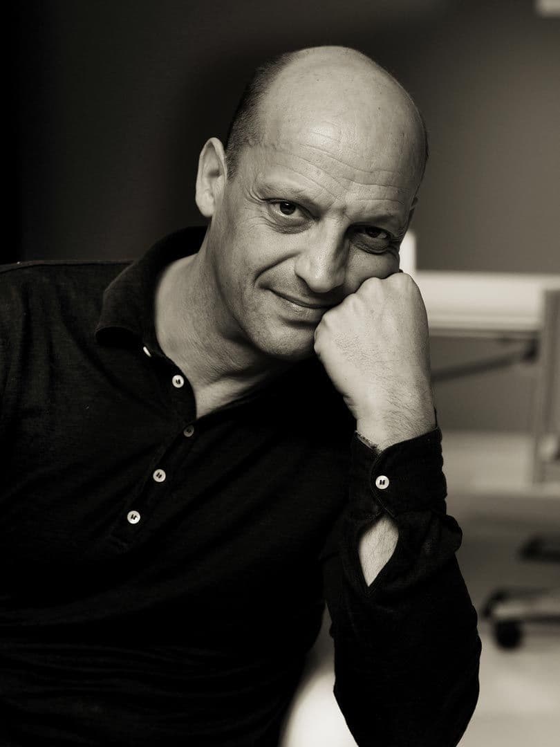 Black and white portrait of a smiling bald man with a beard, resting chin on hand.