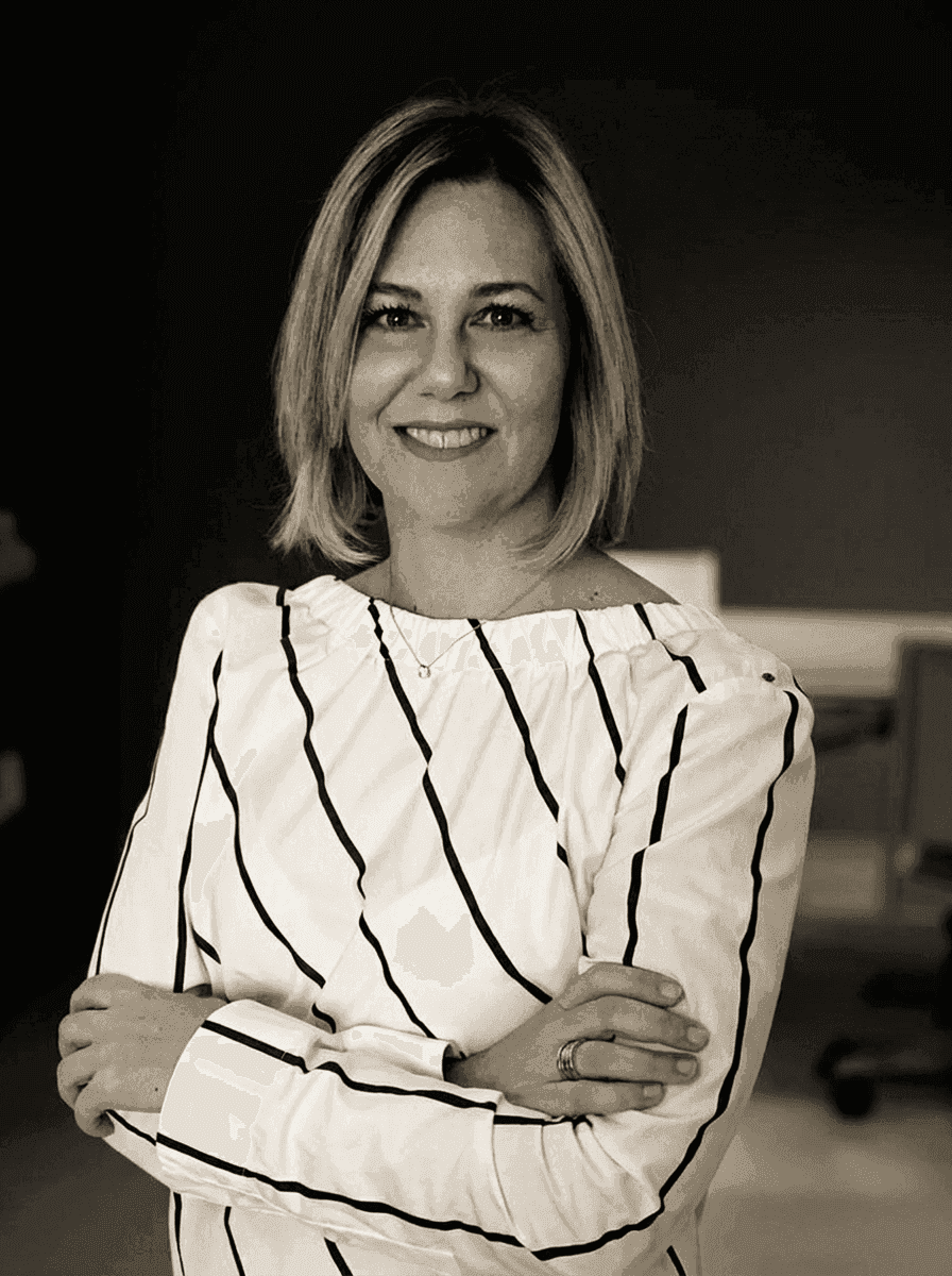 Black and white portrait of a smiling woman with blonde hair, striped shirt, arms crossed.